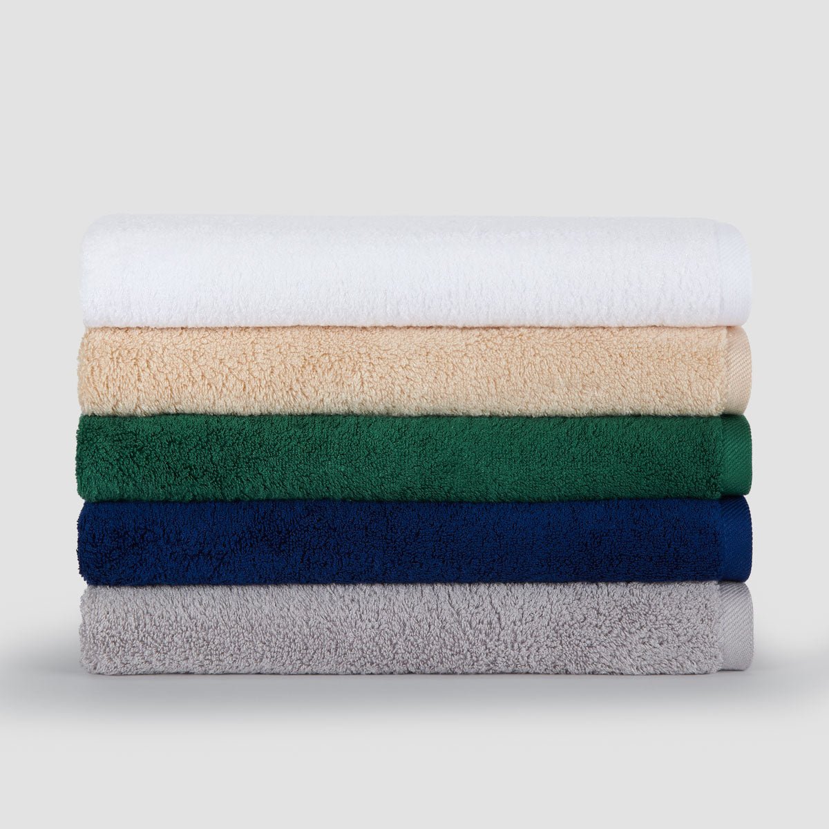 Stapel van vijf gevouwen bamboe handdoeken in wit, beige, groen, marineblauw en grijs tegen lichte achtergrond.