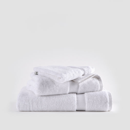 White bamboo towel set stacked neatly showing face, hand, and bath towels with textured bands against neutral background.