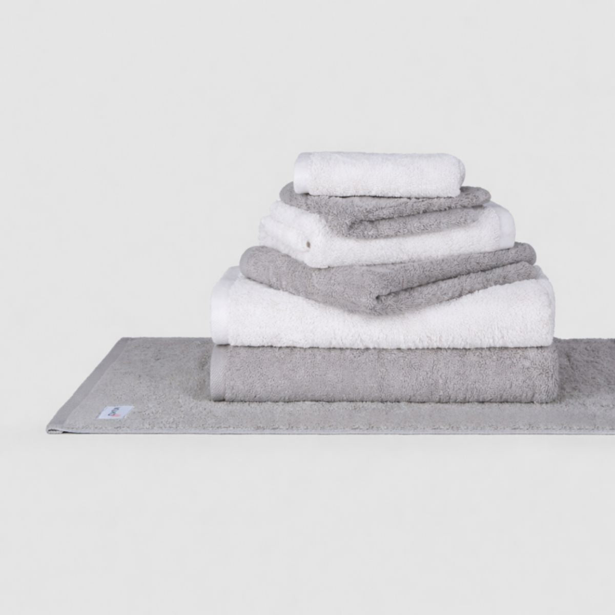 Wabi Sabi towel set by Momo Cotton displayed in stacked gray and white towels on a folded base towel against white background