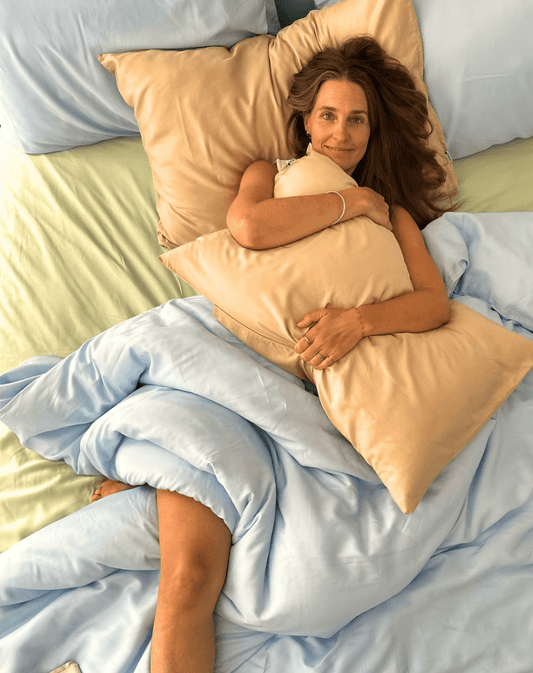 Vrouw in bed met perzik katoenen lakenstel met blauw dekbed, lichtgroen laken zichtbaar eronder