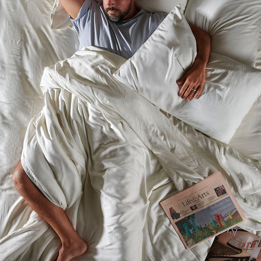 Homem dormindo em jogo de cama de bambu branco com almofada e edredom, vista de cima com jornal