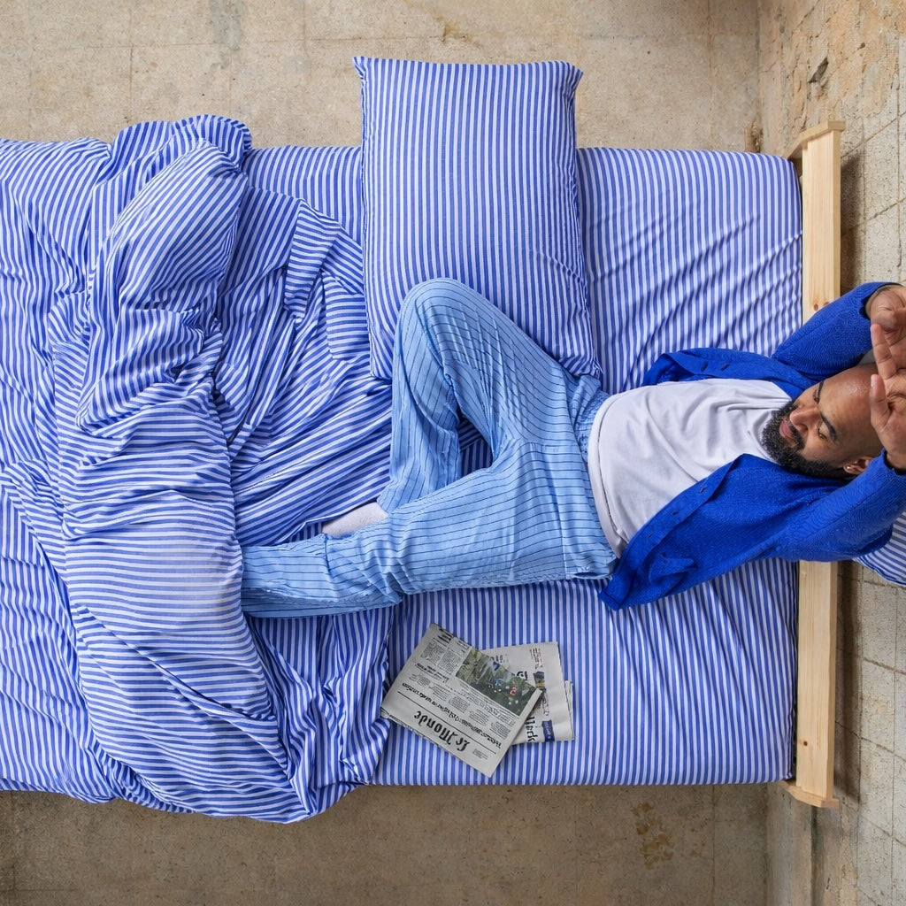Man lying on blue and white patterned duvet cover in bed with newspaper, overhead view