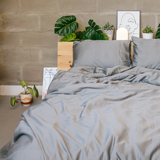 Capa de edredão em bambu cinzento na cama com almofadas, plantas e decoração de quarto minimalista