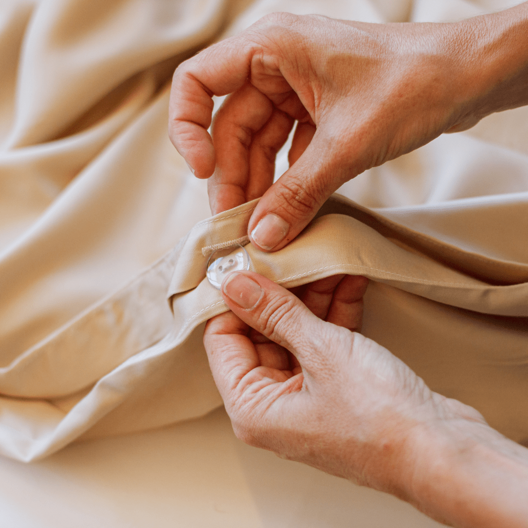Handen die zachte beige katoenen beddengoed en handdoeken van de Momo Cotton complete linnencollectie aanraken