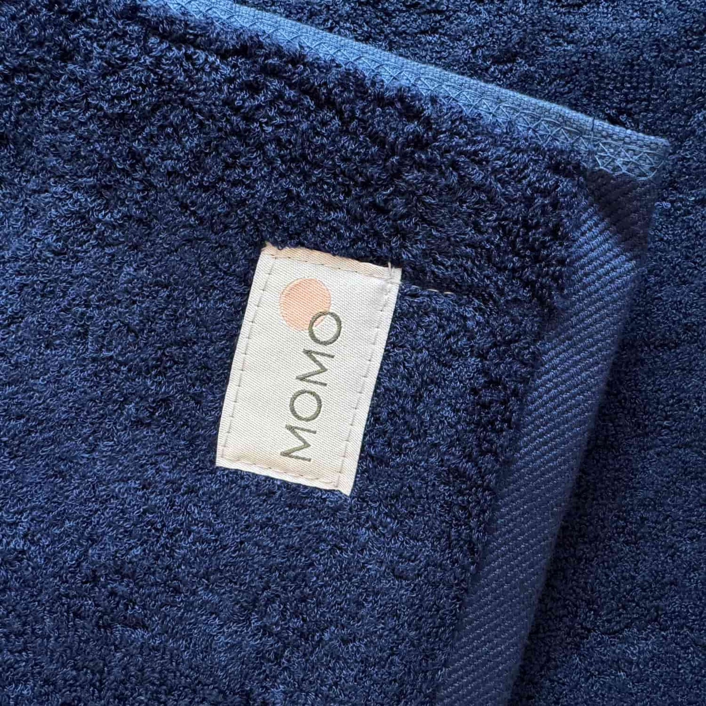 Donkerblauwe Wabi-sabi badmat van Momo Cotton met zichtbaar merklabel op gestructureerde stofoppervlak