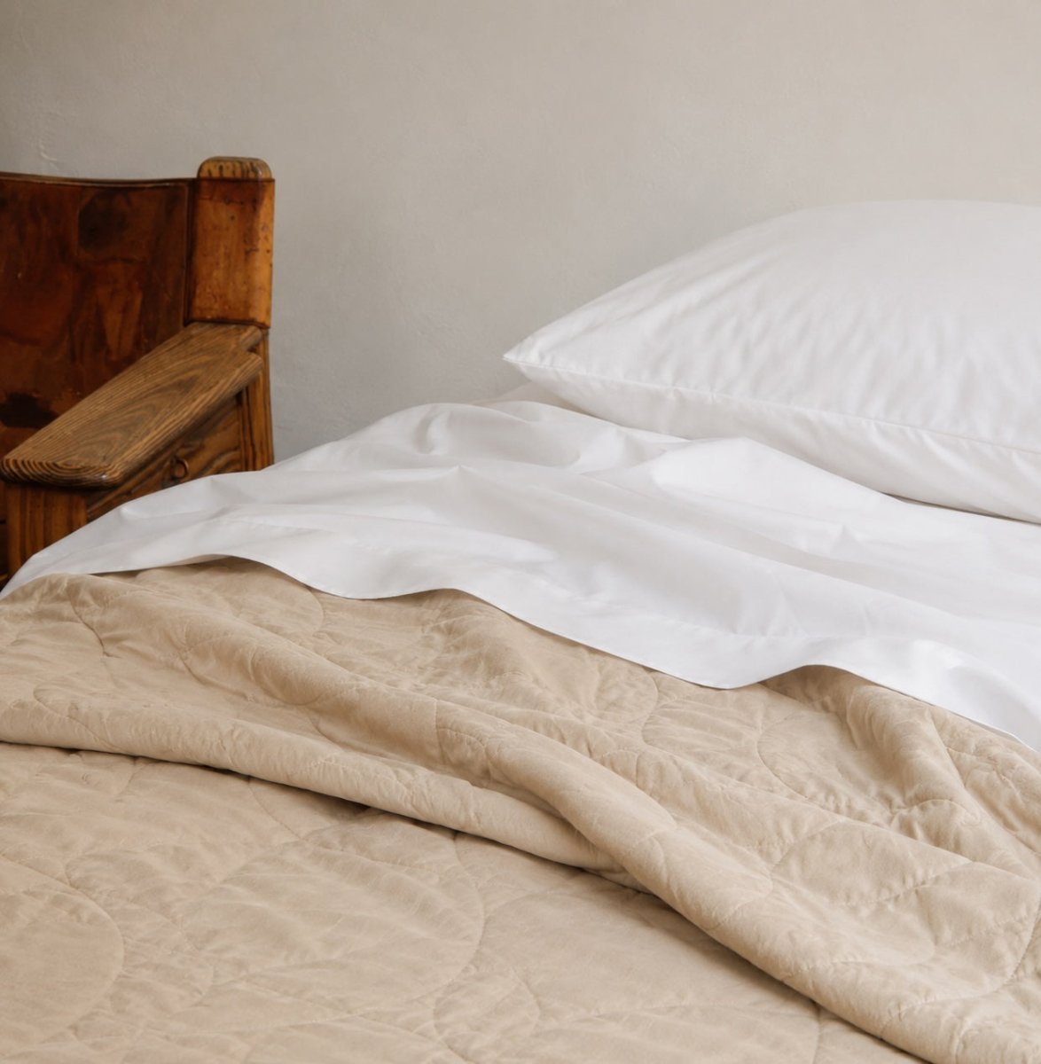 Beige gequilte zomersprei gelaagd op witte lakens met kussens op houten bedframe