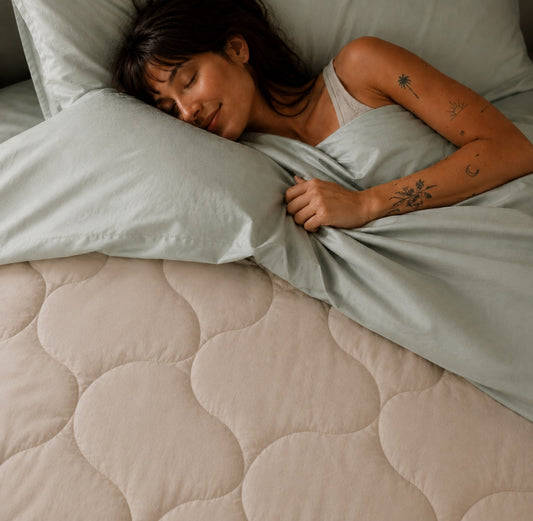 Woman sleeping peacefully on bed with beige quilted comforter and light gray sheets by Momo Cotton