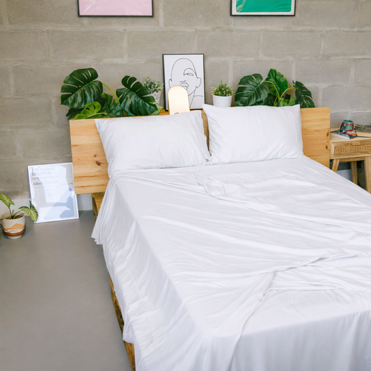 Lençol de bamboo branco exibido em cama de estrutura de madeira com plantas verdes e decoração minimalista do quarto