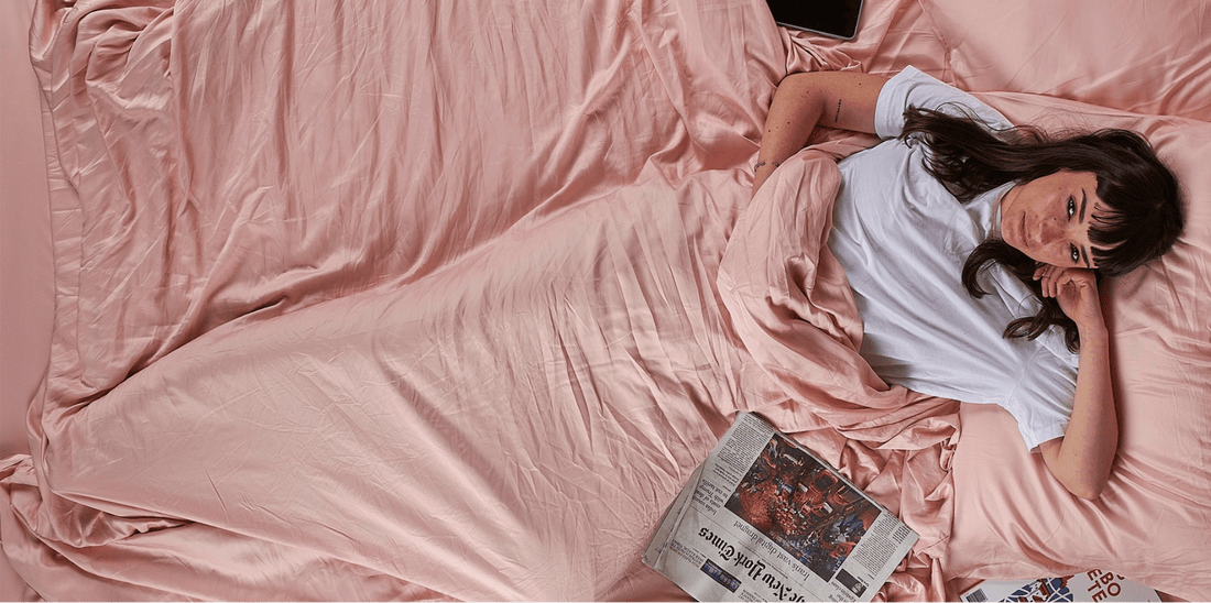 Vrouw liggend op bed met roze beddengoed krant lezend, lenteslaapkamerdecoratie.