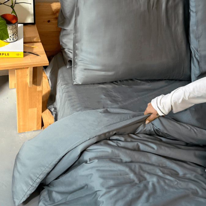 Vrouw aanraakend grijze bamboe beddengoed op bed met houten tafel op de achtergrond