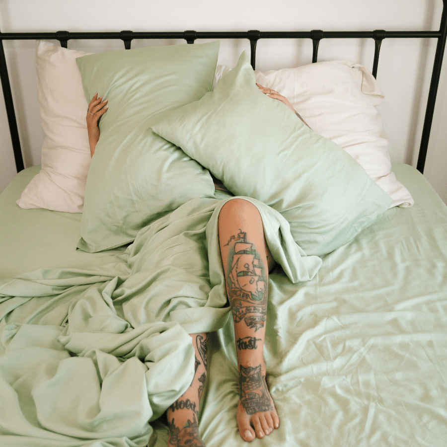 Persoon in bed met groen-wit bamboe beddengoed en zichtbare tatoeages op de benen