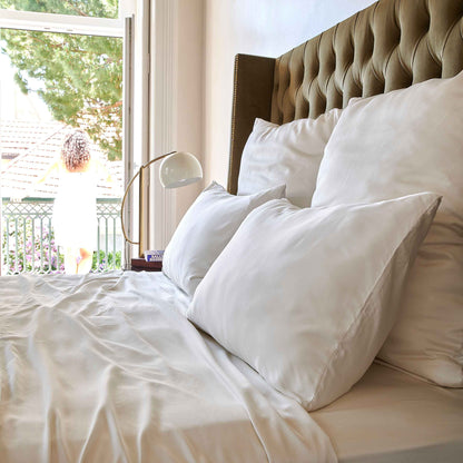 Wit beddengoed op bed met gestoffeerd hoofdeinde bij raam met uitzicht op tuin