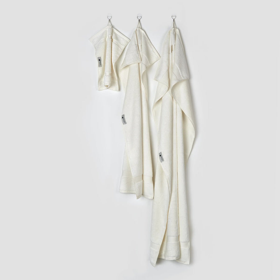Drie crèmekleurige bamboe handdoeken aan haakjes met gezichts-, hand- en badformalaten uit de Alba-collectie van momo-cotton