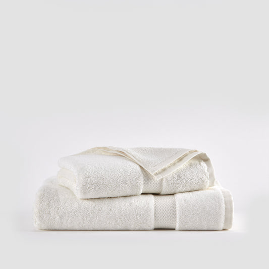 Three cream-colored bamboo towels stacked on white background - face, hand, and bath towel set