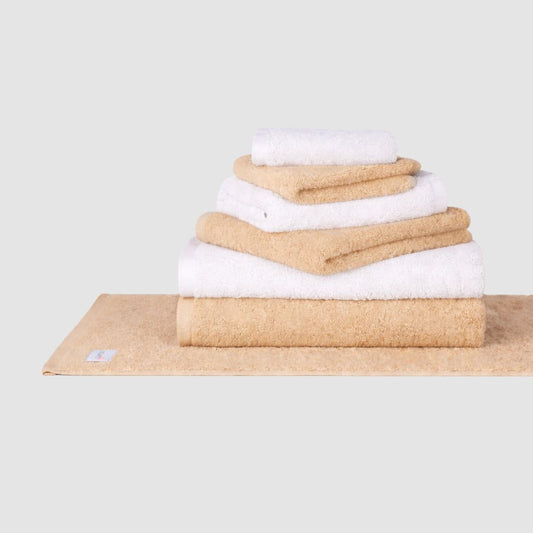 Gestapelde set beige en witte katoenen handdoeken van Momo Cotton op neutrale achtergrond