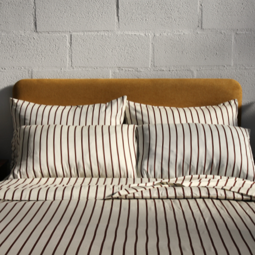 Jogo de cama completo de bambu com fronhas e lençóis listrados em branco e cinzento sobre cama com cabeceira castanha.