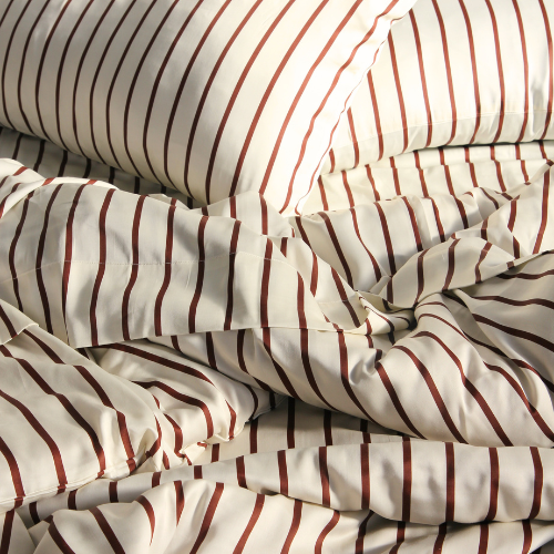 Bamboe dekbedovertrekset met rood-beige strepenpatroon op onopgemaakte bed, zijdeachtige textuur zichtbaar