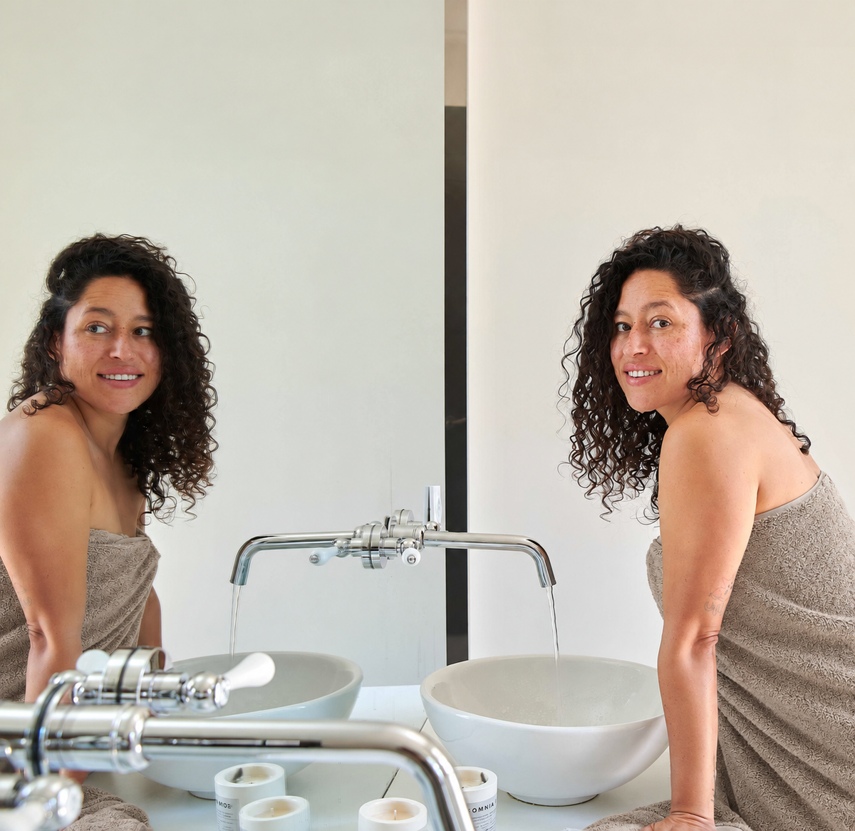 Woman wrapped in beige bamboo towel in front of bathroom mirror