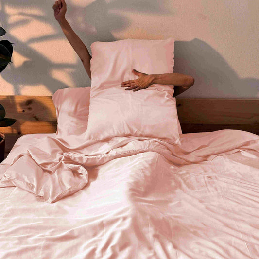Woman in bed with pink bamboo sheets and pillows – soft, breathable and sustainable bedding