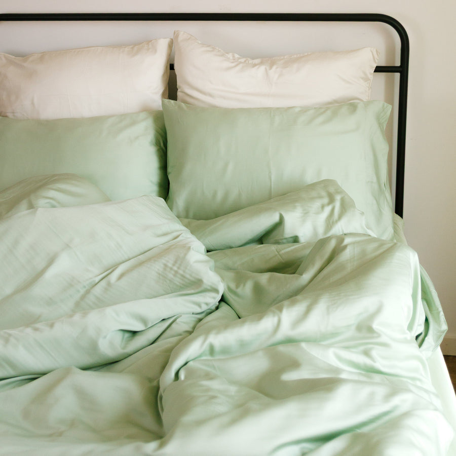 Lichtgroen en wit dekbedovertrekset op bed met zwart frame, wanddecoratie met rieten borden