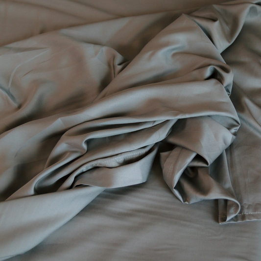 Jogo de lençol em bambu bege dobrado, mostrando textura macia e trama lisa da coleção de roupa de cama completa.