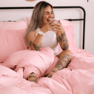 Vrouw ligt comfortabel op roze bamboe lakens, benadrukt de zijdeachtige textuur en zachte vouw.
