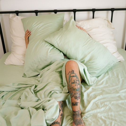 Jogo de cama Momo em algodão verde sálvia e branco exibido em cama com cabeceira de metal preto