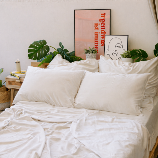 Jogo de cama em bambu branco exibido na cama com almofadas, plantas e arte na decoração do quarto